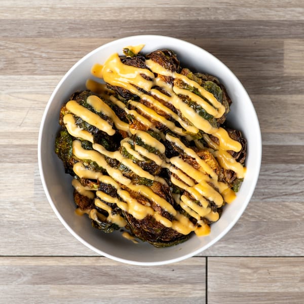 A white bowl filled with crispy Brussels sprouts drizzled with a creamy orange sauce.