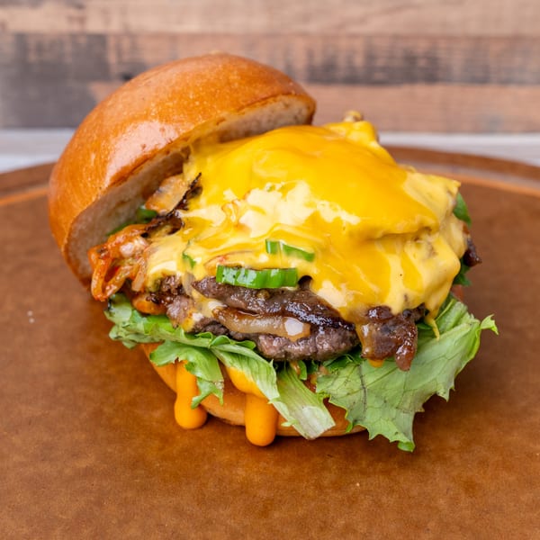 A Standing Room burger with melted cheese, grilled onions, jalapeños, and lettuce on a bun.