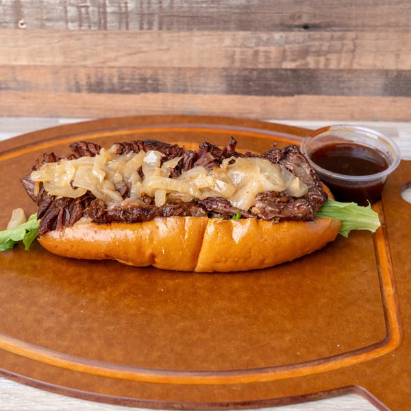 A Standing Room burger with shredded beef, caramelized onions, and lettuce on a bun, with a side of sauce.
