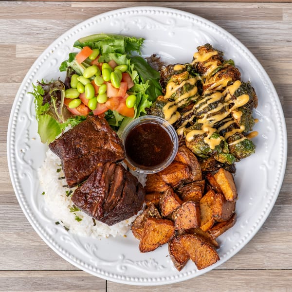 A plate of short ribs with rice, roasted potatoes, Brussels sprouts, and a side salad.