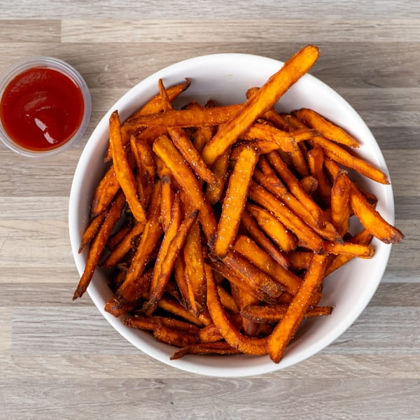 A white bowl filled with crispy sweet potato fries and a side of ketchup on a wooden table.