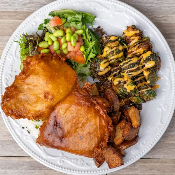A plate of crispy fried chicken, roasted Brussels sprouts with sauce, sweet potatoes, and a side salad.