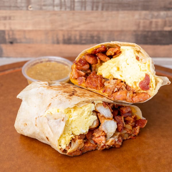 A breakfast burrito, cut in half, revealing scrambled eggs, sausage, and bacon, with a side of salsa.