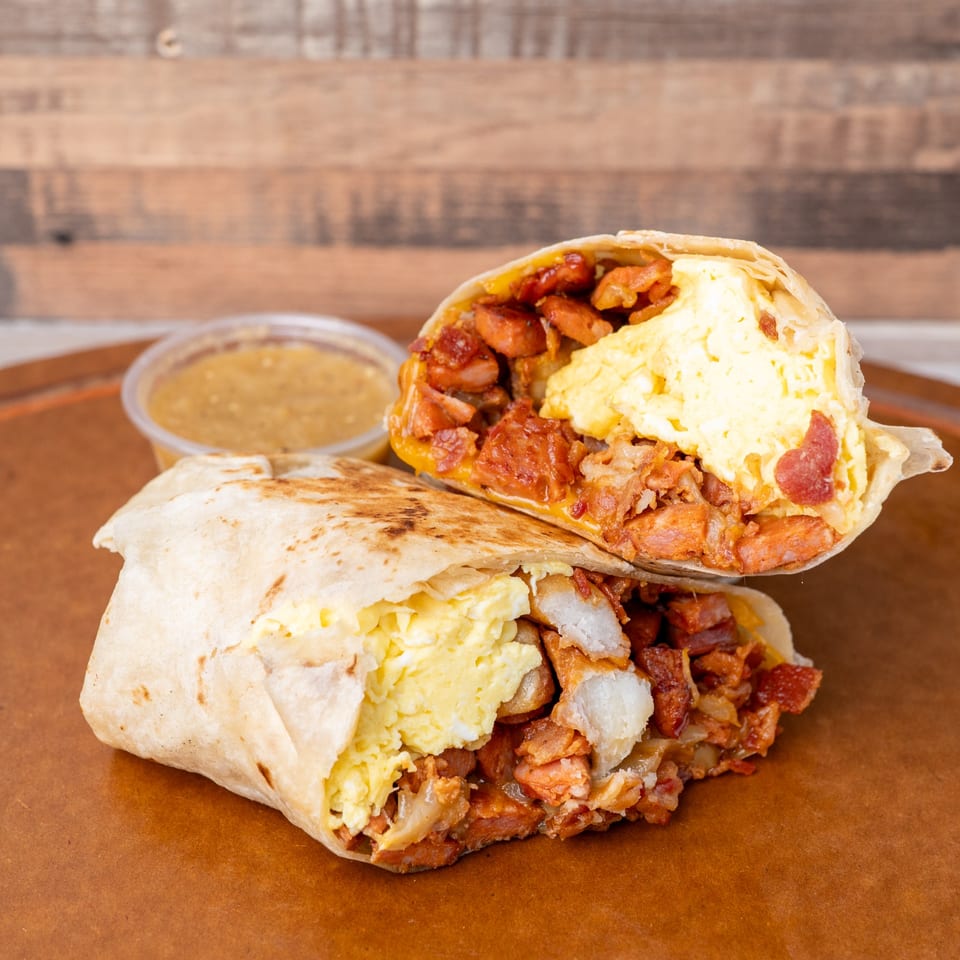 A breakfast burrito, cut in half, revealing scrambled eggs, sausage, and bacon, with a side of salsa.