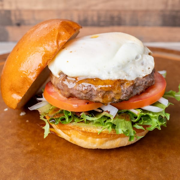 A Standing Room burger with a fried egg, patty, tomato, onion, and lettuce on a bun.