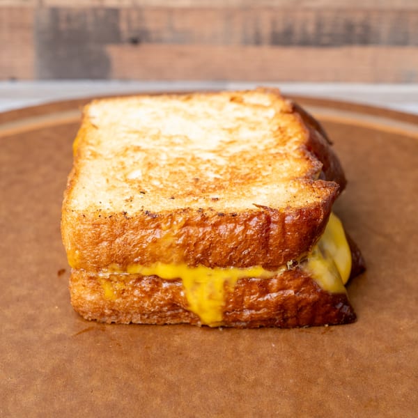 A grilled cheese sandwich with melted yellow cheese oozing out, served on brown paper.
